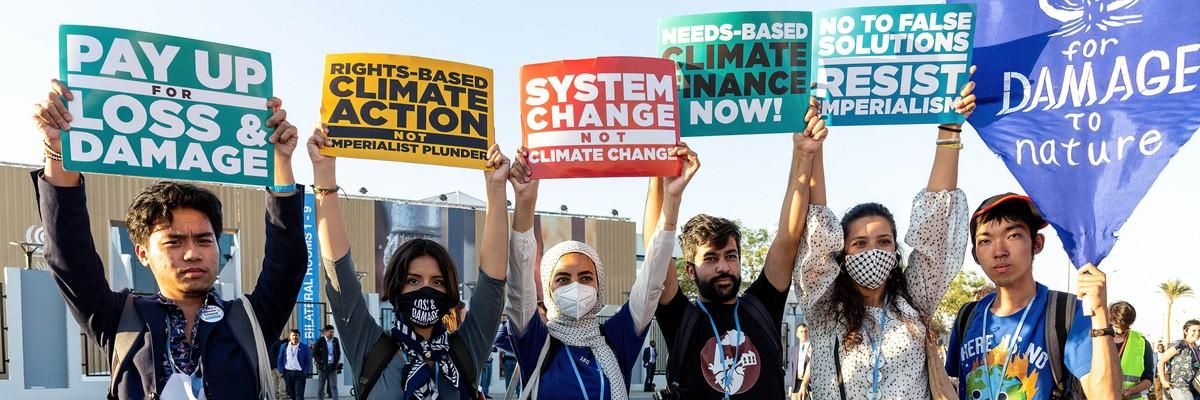 Six protestors hold signs demanding loss and damage reparations.