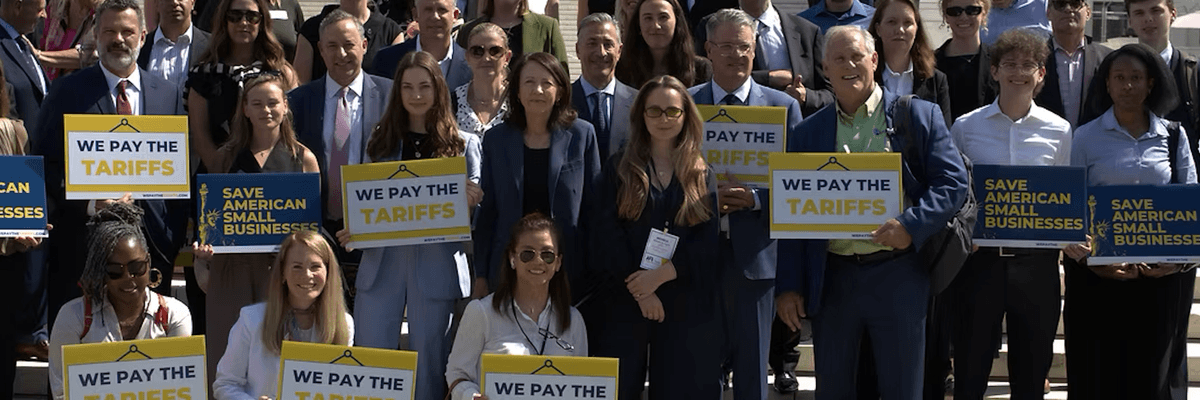 Small business owners hold signs reading "we pay the tariffs"