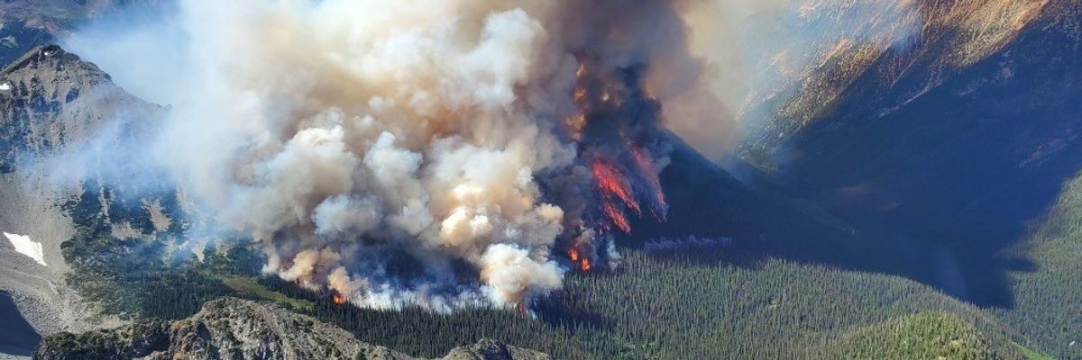Smoke and flames from a wildfire erupts from a tree-covered mountain .