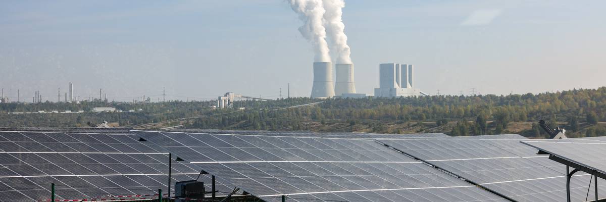 Solar panels in front of a smoke stack.