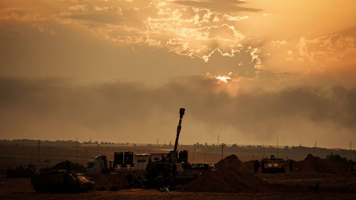 Soldiers from an artillery unit stand in front of a gunsmoke-polluted sky.