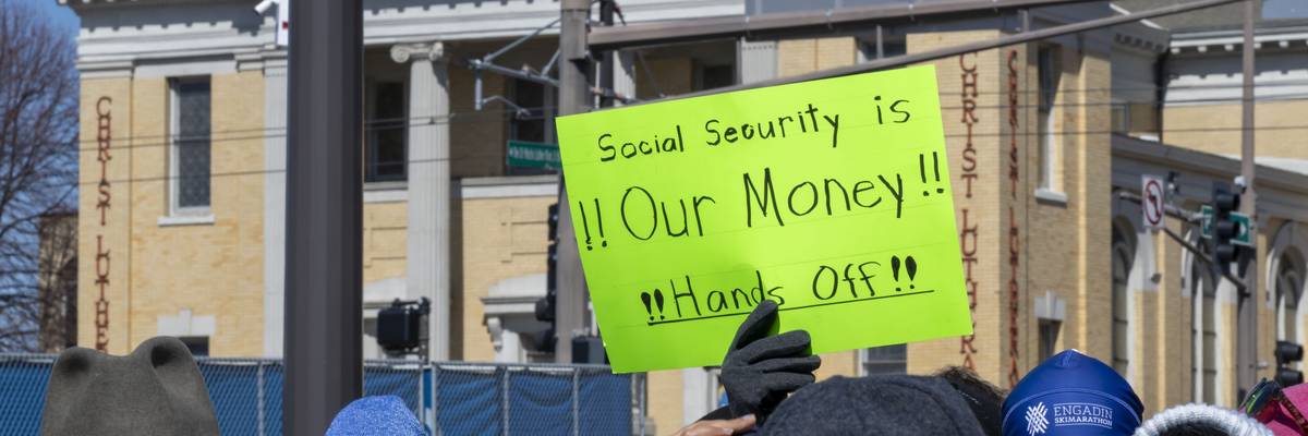 Someone holds neon green sign reading, "Social Security Is Our Money! Hands off!"