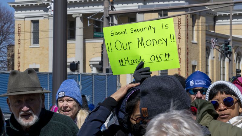 Someone holds neon green sign reading, "Social Security Is Our Money! Hands off!"