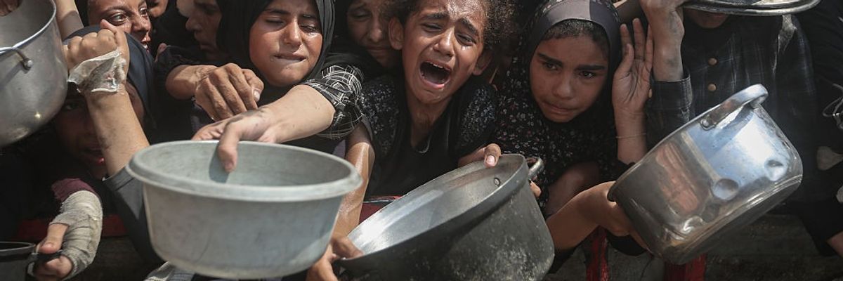Starving Palestinians wait to receive food distributed by a charity