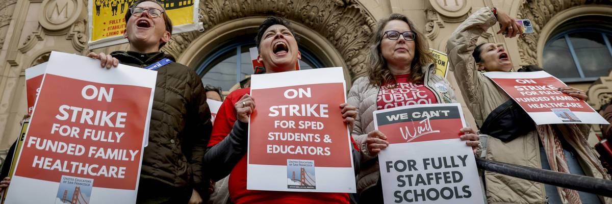 Striking San Francisco teachers hold signs reading, "On Strike for Fully Funded Family Healthcare" and other messages