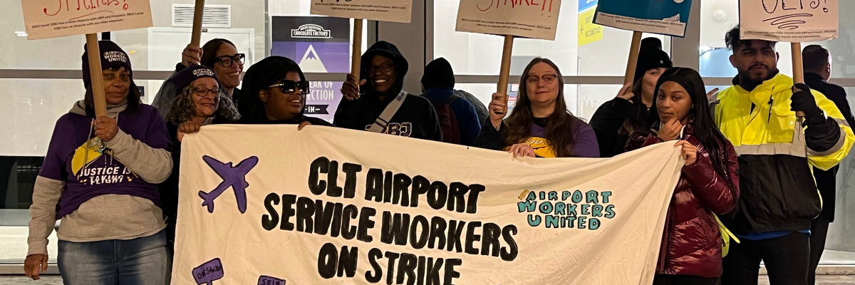 Striking workers hold a up a sign that says "CLT Airport Service Workers on Strike"
