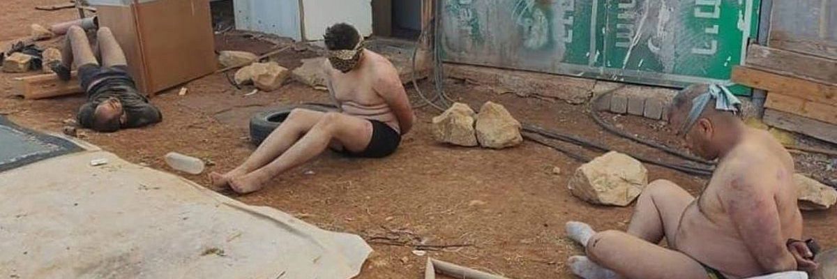 Stripped, blindfolded, and bound Palestinian men detained by Israeli forces sit on the ground 