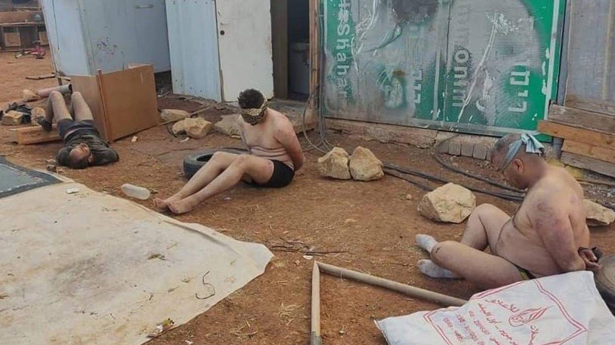 Stripped, blindfolded, and bound Palestinian men detained by Israeli forces sit on the ground