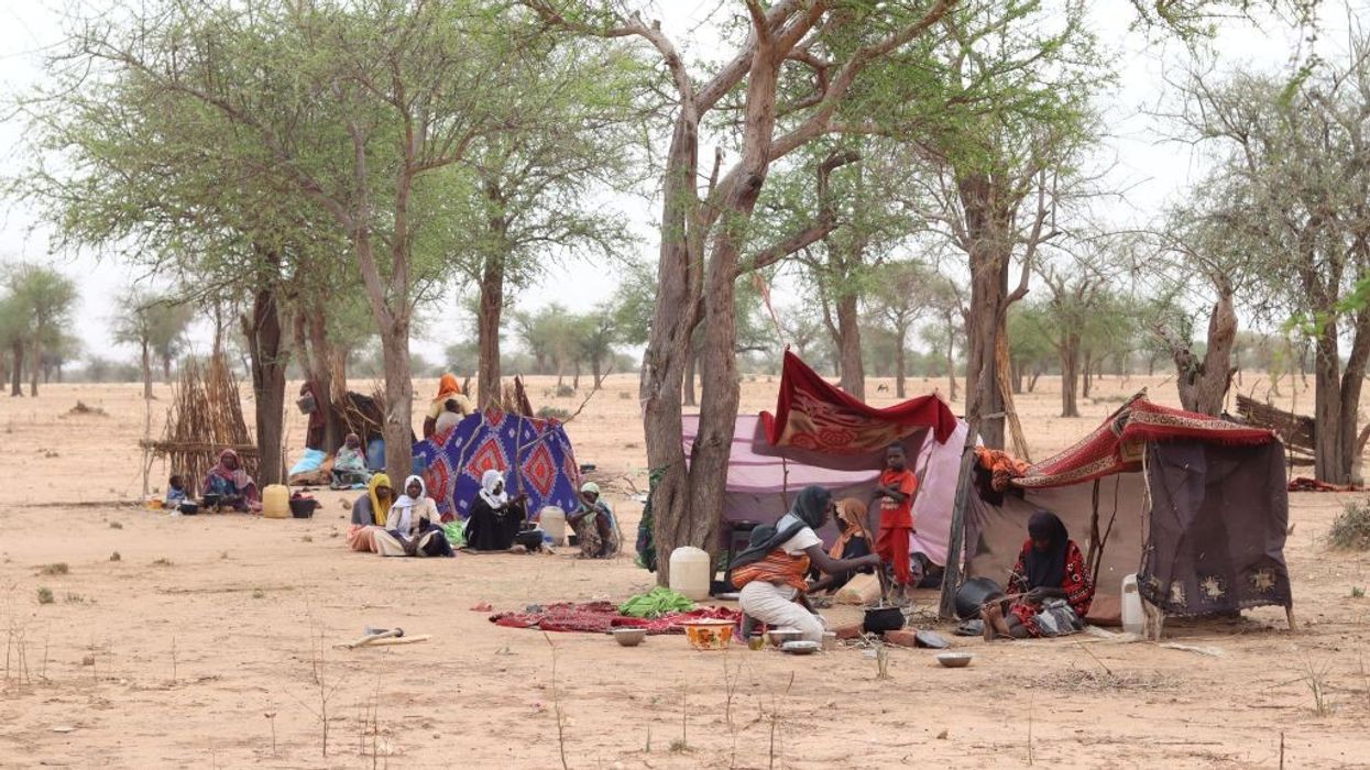 Sudanese refugees in cloth tents set up below trees on parched earth.
