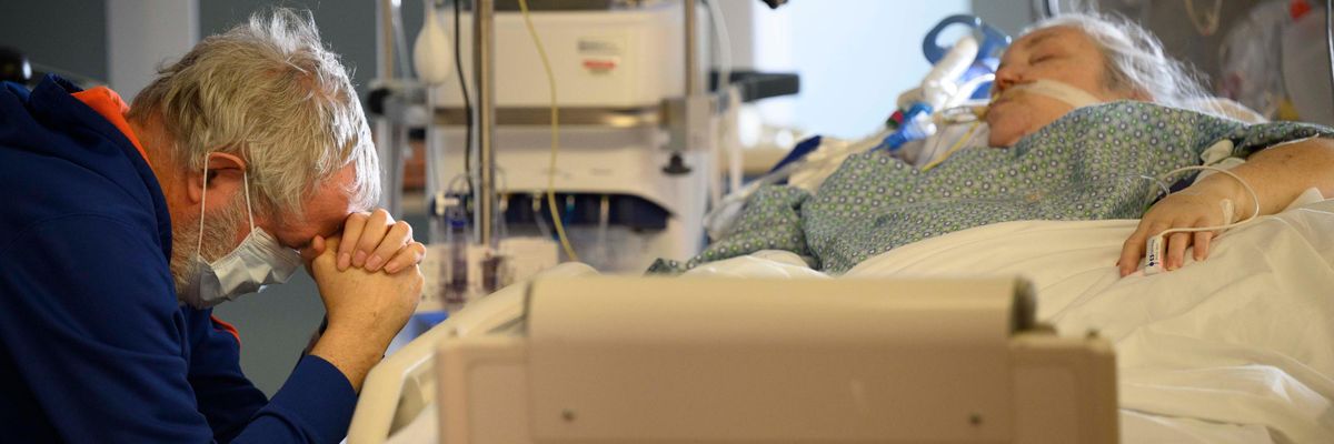 The husband of a Covid-19 patient prays at her bedside