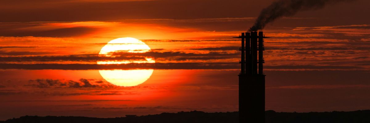 the sun is setting behind a smoke stack