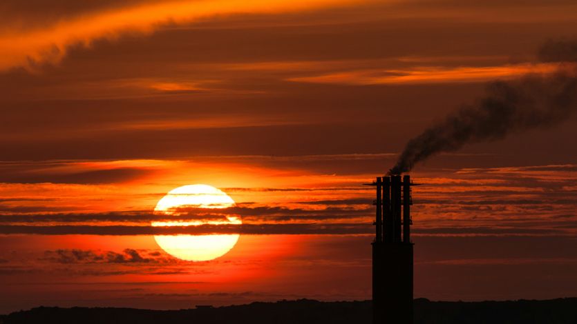 the sun is setting behind a smoke stack