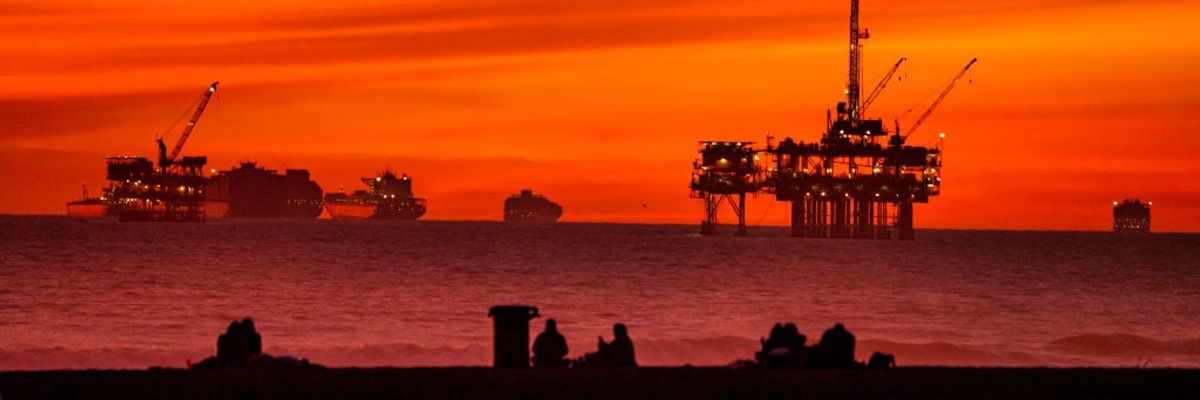 The sun sets over container ships and oil platforms off the coast of Huntington Beach