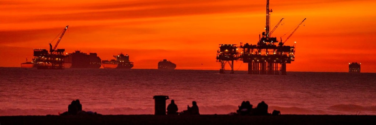 The sun sets over container ships and oil platforms off the coast of Huntington Beach