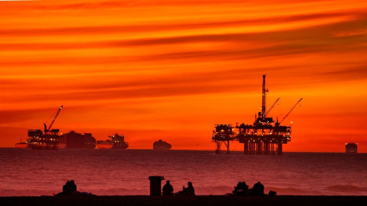 The sun sets over container ships and oil platforms off the coast of Huntington Beach