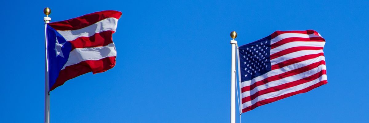 The U.S. and Puerto Rican flags flap against a blue sky.