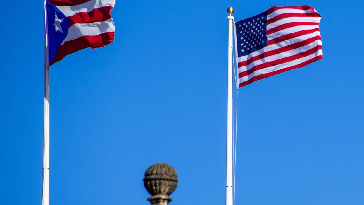 The U.S. and Puerto Rican flags flap against a blue sky.