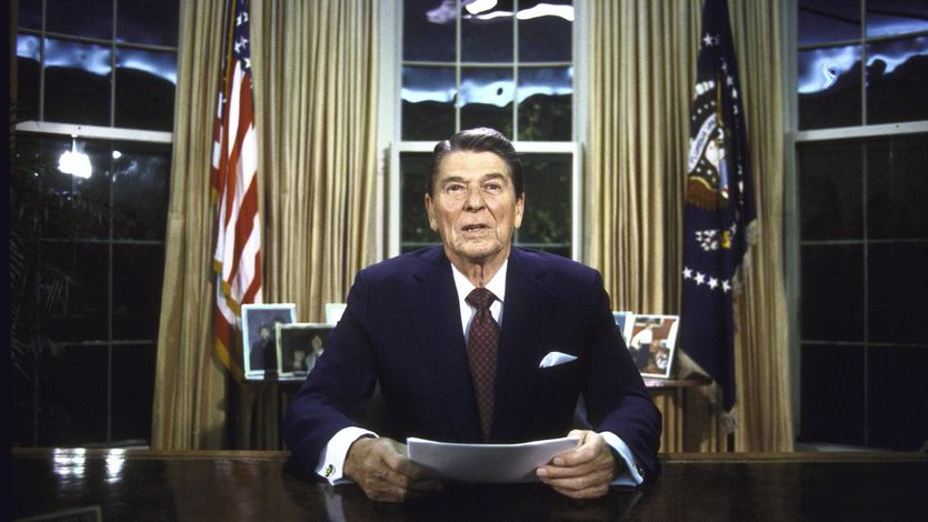 Then-President Ronald Reagan seated at his desk in the Oval Office