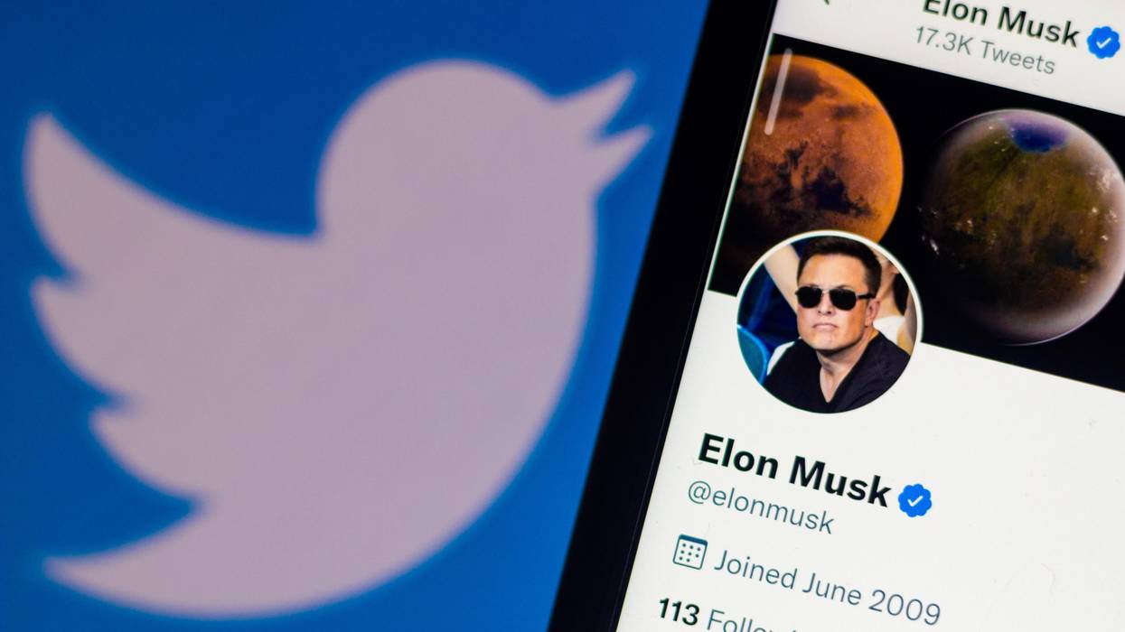 This photo illustration shows the Twitter logo behind a smartphone with Elon Musk's official profile on April 11, 2022.