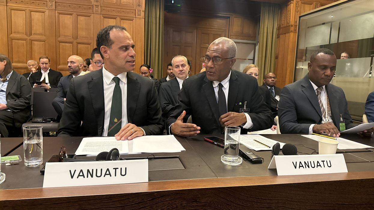 Three men in suits sit at a table.