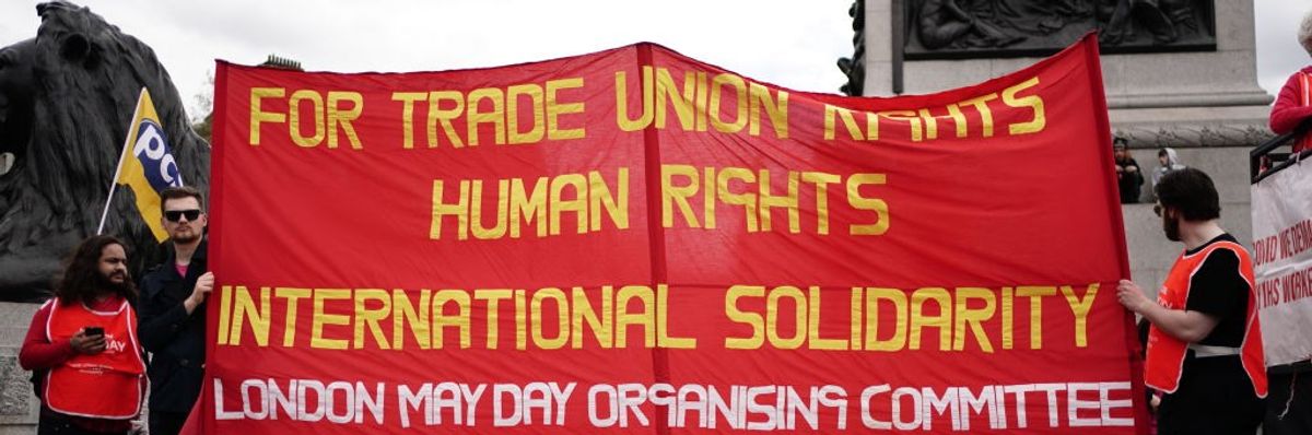 Three people hold up a red banner with yellow and white writing. 