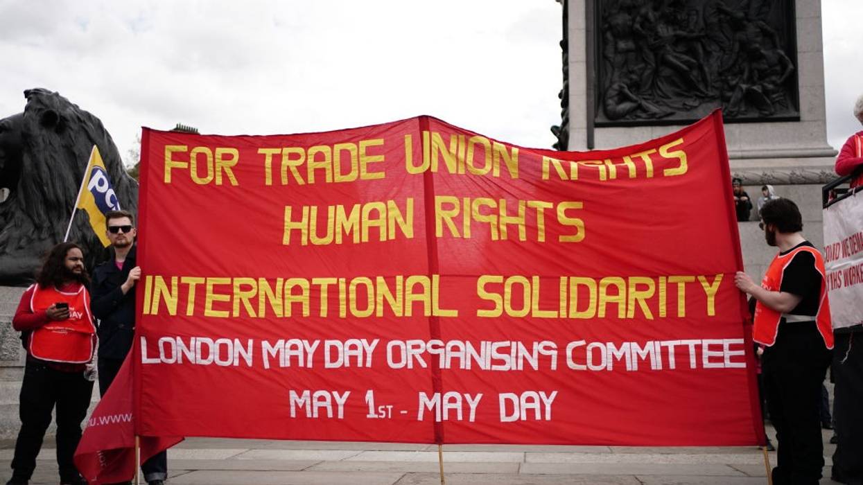 Three people hold up a red banner with yellow and white writing.