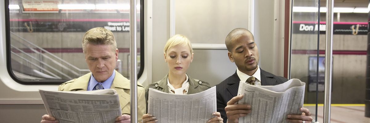 Three people on a subway train read newspapers. ​