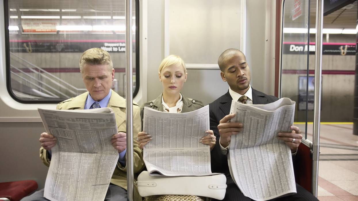 Three people on a subway train read newspapers. 