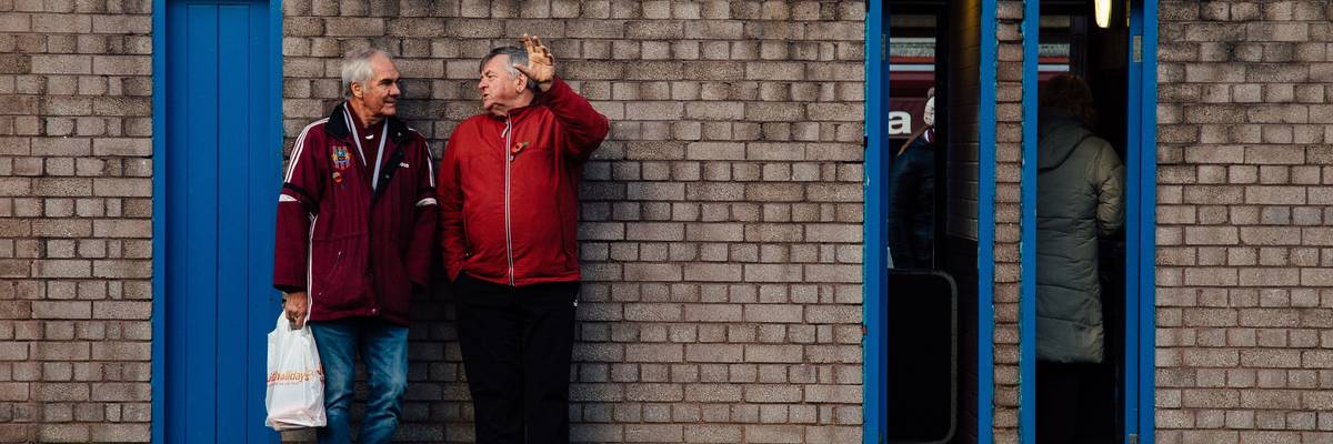 To older men lean against a brick wall talking.