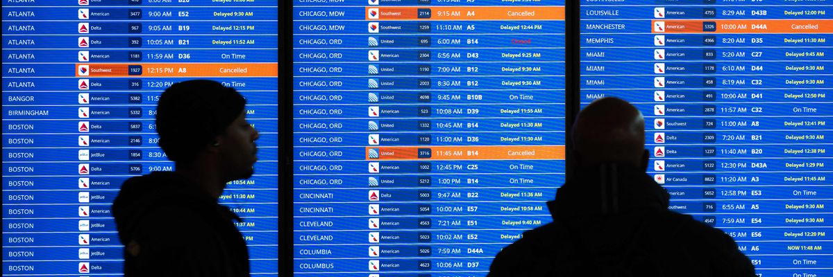 Travelers look at a flight information display listing canceled and delayed flights