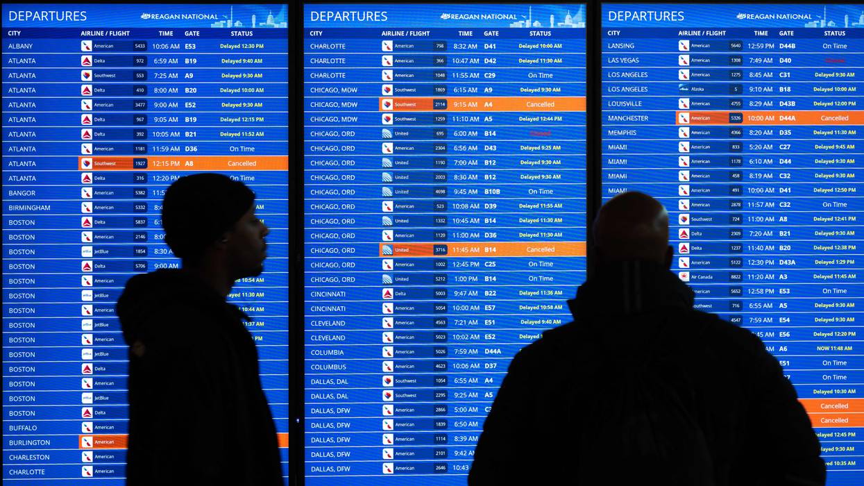 Travelers look at a flight information display listing canceled and delayed flights