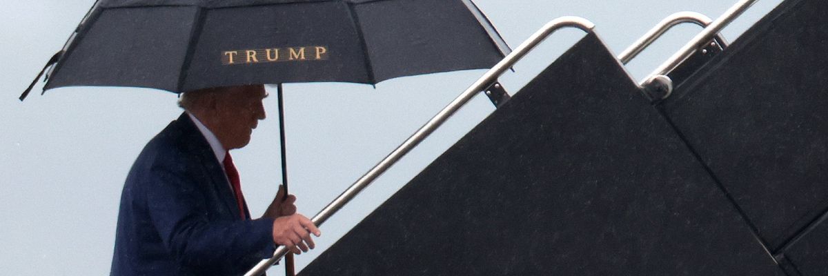 Trump climbs up plane steps holding umbrella with his name on it