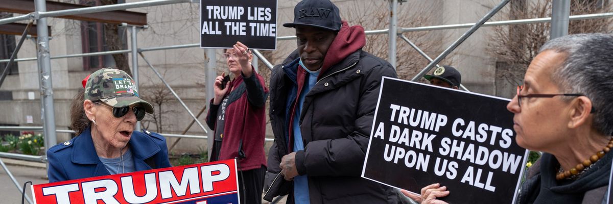Trump protester and supporter hold opposing signs outside New York courthouse.