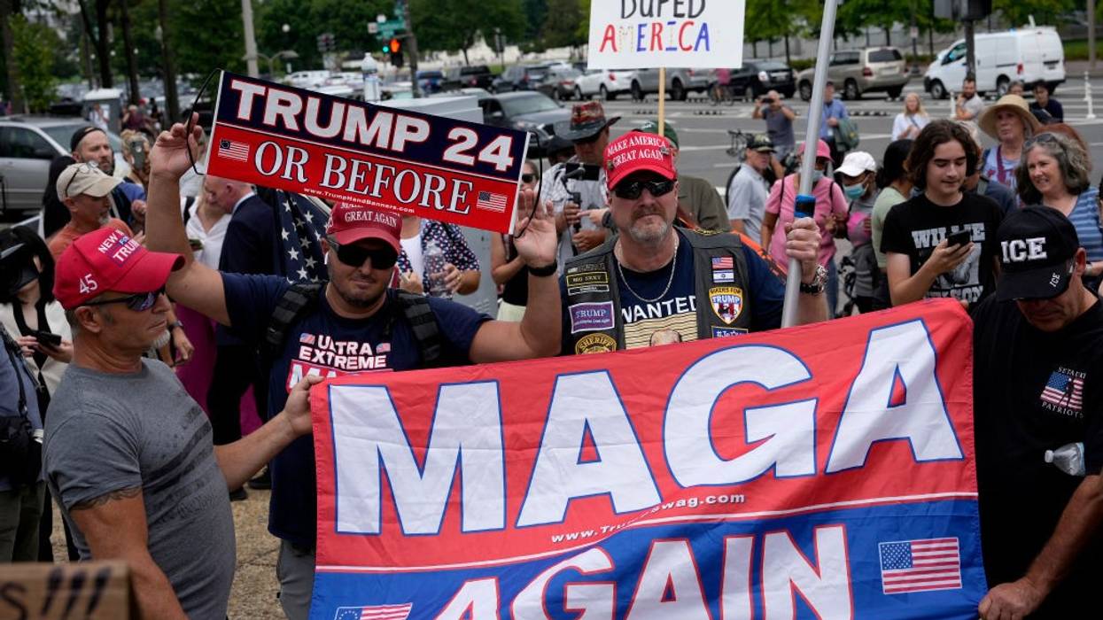 Trump supporters with signs and a banner reading MAGA.