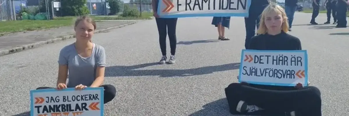 Two activists sit in a road with signs while two more stand behind them with a banner.