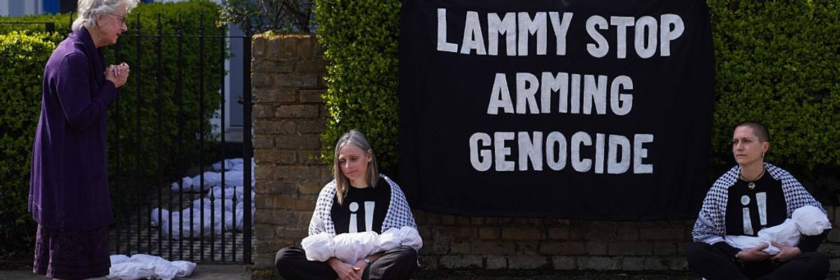 Two activists sit with models of dead babies on either side of words reading, "Lammy Stop Arming Genocide."