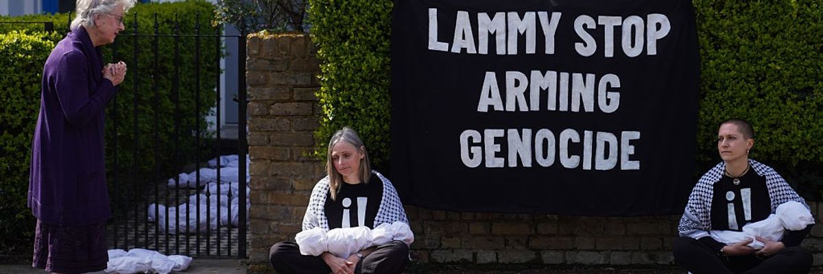 Two activists sit with models of dead babies on either side of words reading, "Lammy Stop Arming Genocide."