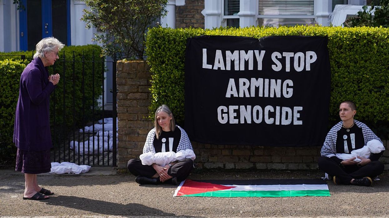 Two activists sit with models of dead babies on either side of words reading, "Lammy Stop Arming Genocide."