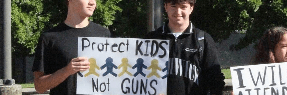 two boys hold a sign reading, "Protect Kids Not Guns"