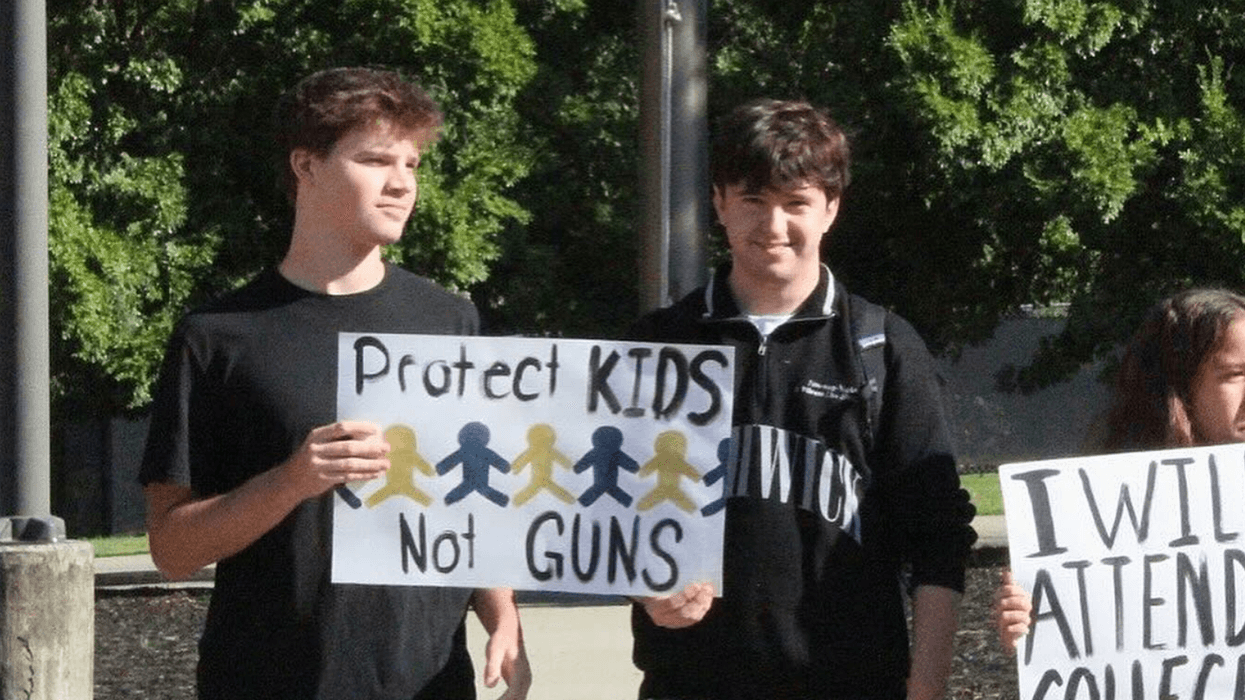two boys hold a sign reading, "Protect Kids Not Guns"