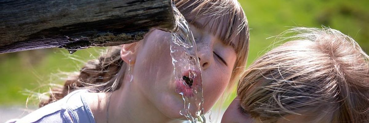 Two children drink water outdoors. 