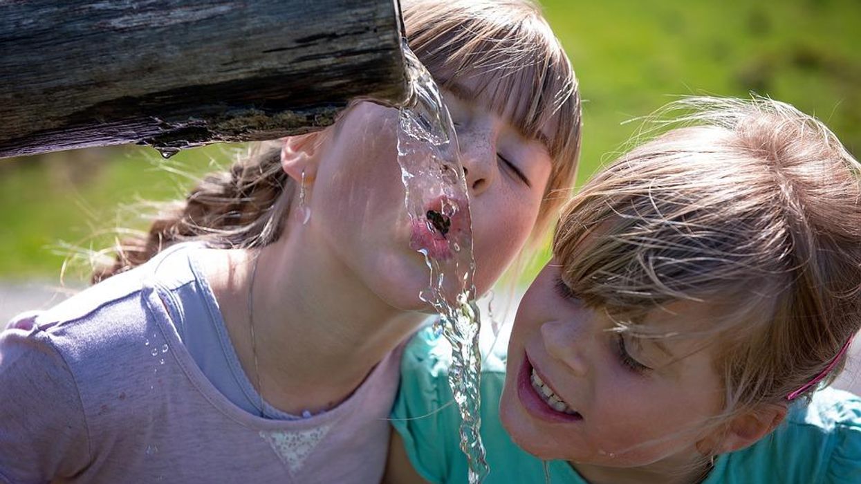 Two children drinking water outdoors. An estimated 110 million Americans are potentially exposed to 'forever chemicals' through drinking water.