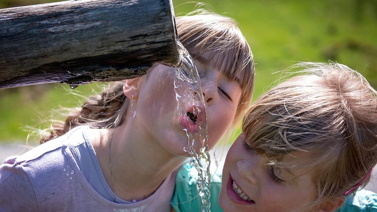 Two children drinking water outdoors. An estimated 110 million Americans are potentially exposed to 'forever chemicals' through drinking water.