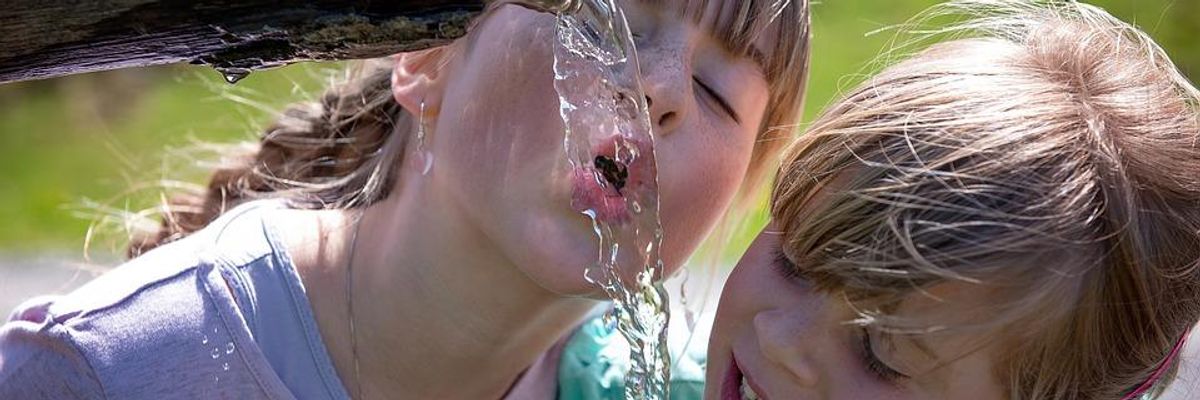 Two children drinking water outdoors. 