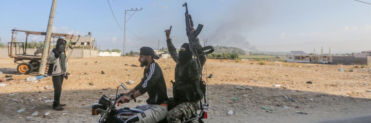 Two figures ride a motorcycle with one holding up a rifle.