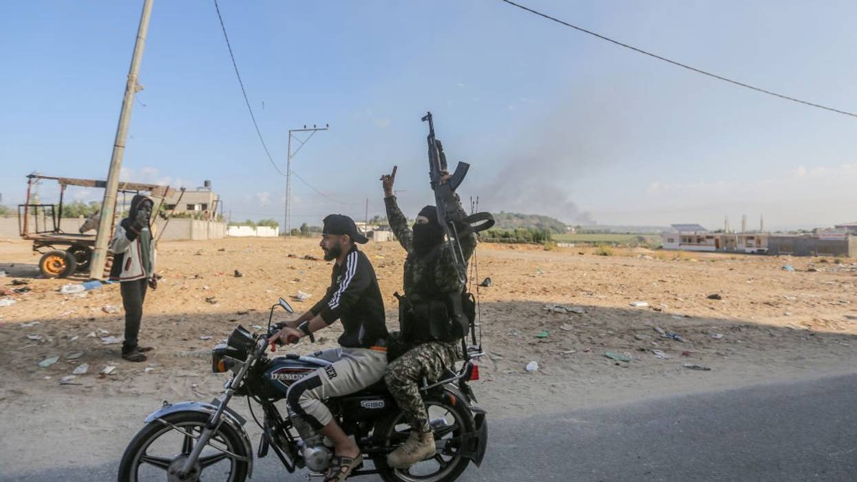 Two figures ride a motorcycle with one holding up a rifle.