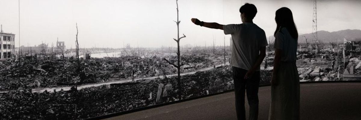 Two figures view a panorama of the aftermath of the atomic bombing of Hiroshima, as one points.