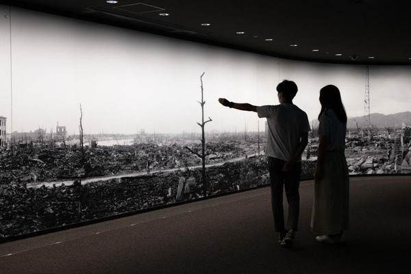 Two figures view a panorama of the aftermath of the atomic bombing of Hiroshima, as one points.