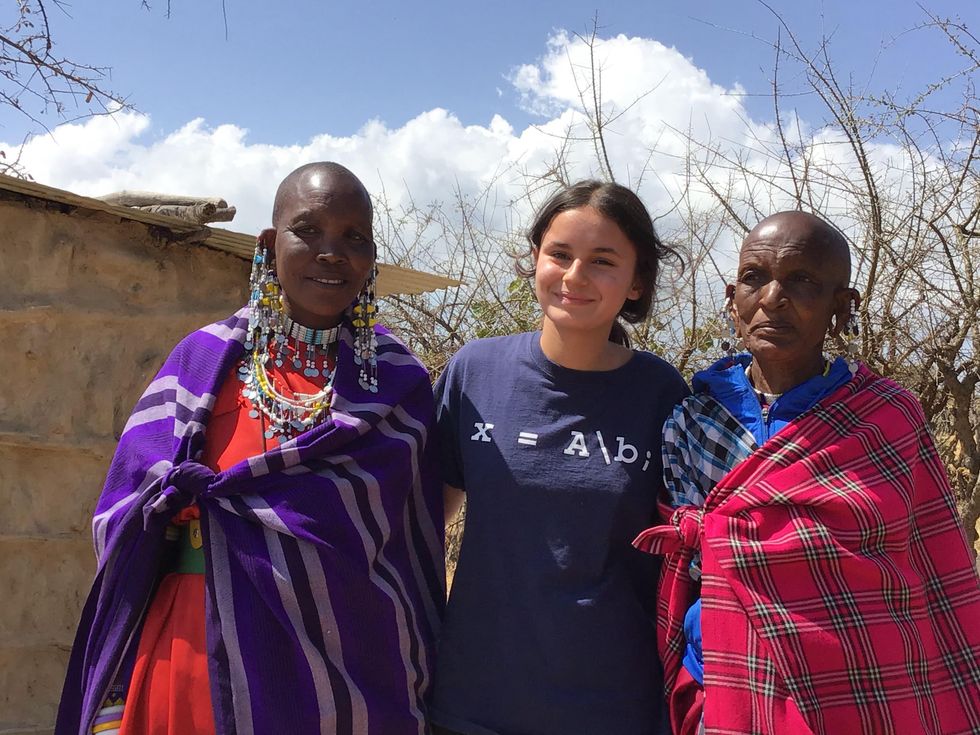 Two Maasai in traditional dress stand with their arms around a young woman in U.S. dress.
