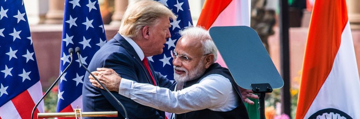 Two men embrace and shake hands in front of flags.